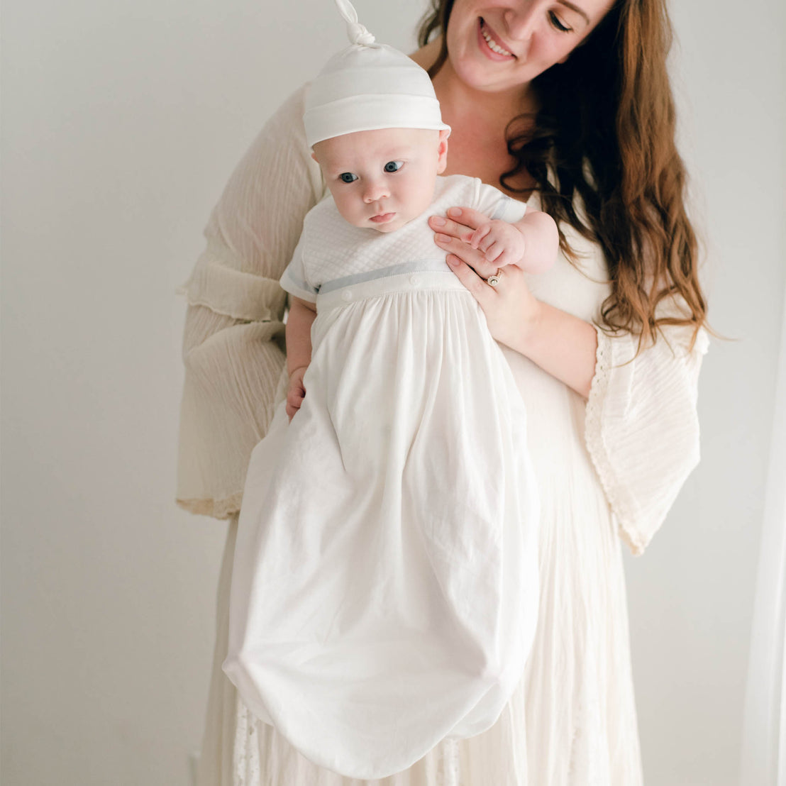 Baby boy being held by his mother. He is wearing the Owen Layette and Knot Cap