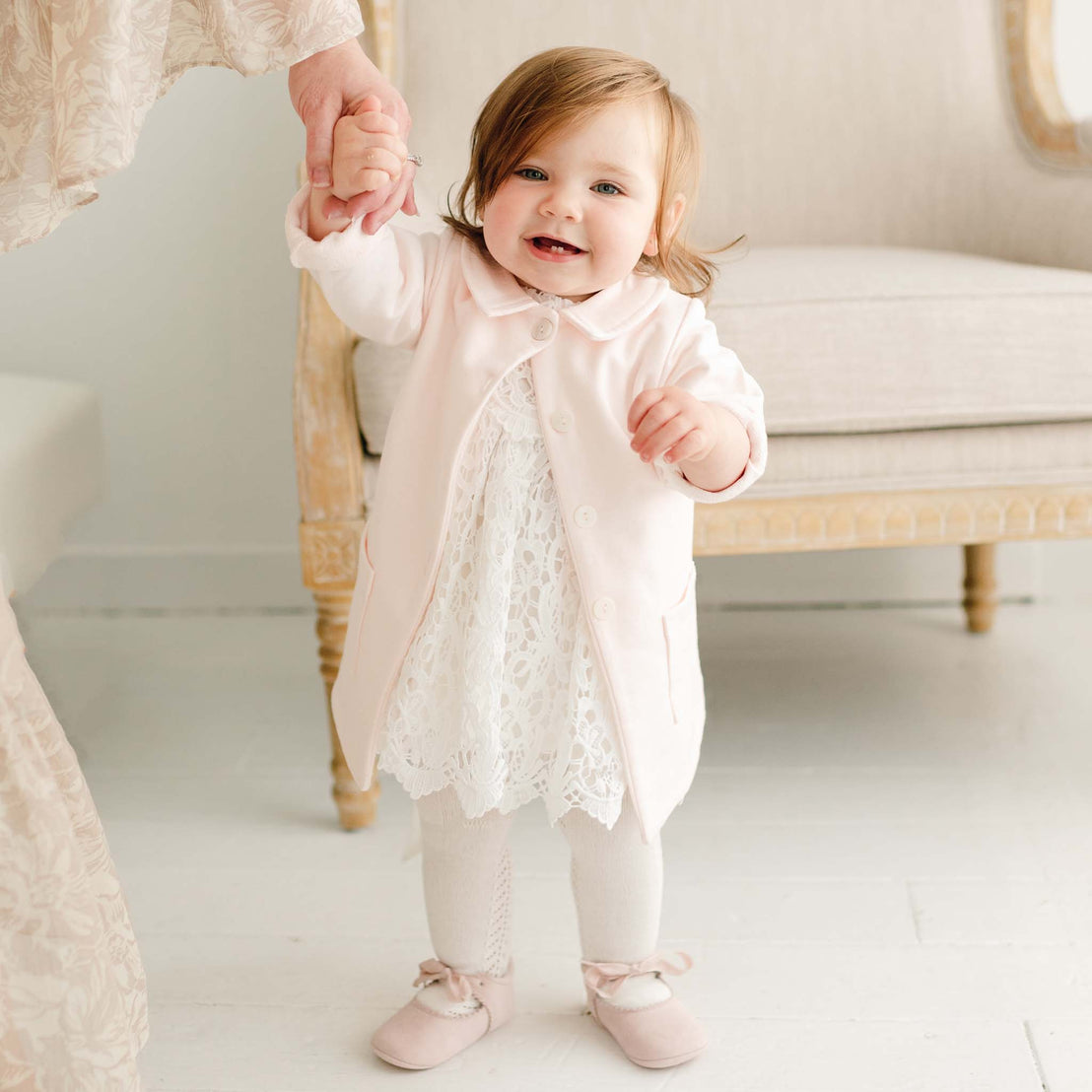 A baby girl wearing the Lola Trench Coat over the Lola Bubble Romper. The coat is made in soft cotton french terry and features buttons and a petite collar. 