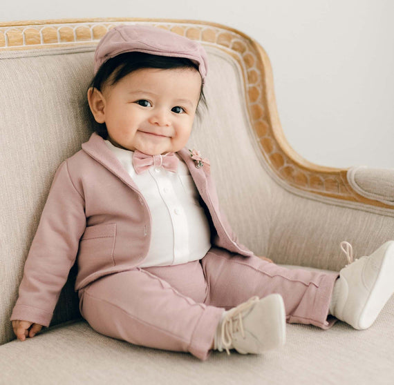 Baby boy sitting in chair in mauve pink suit, hat, tie and tan shoes