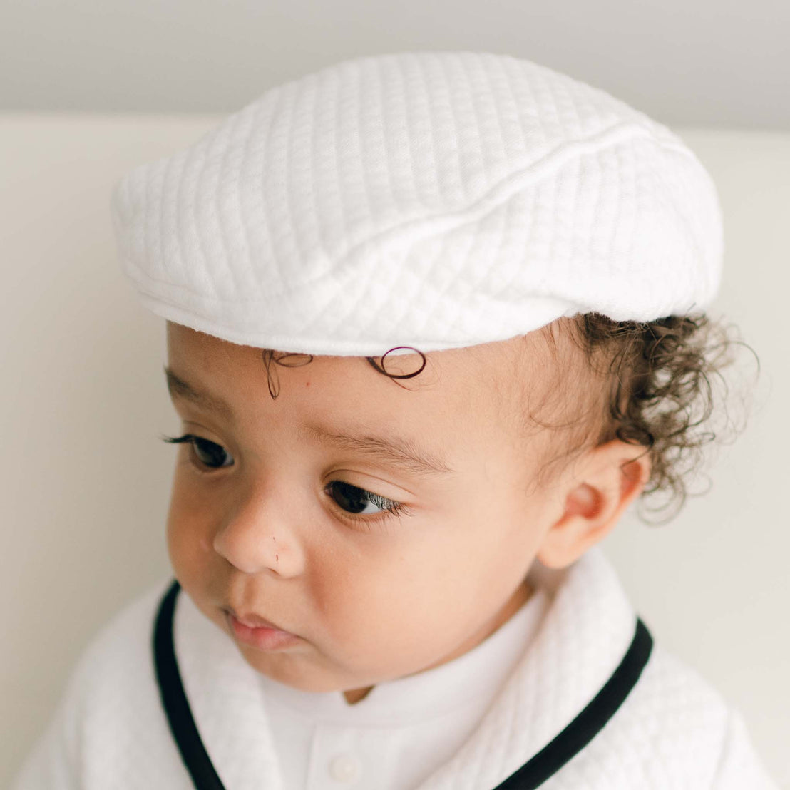 Baby boy wearing the white James Newsboy Cap made from 100% White Quilted Cotton with a soft elastic back. 
