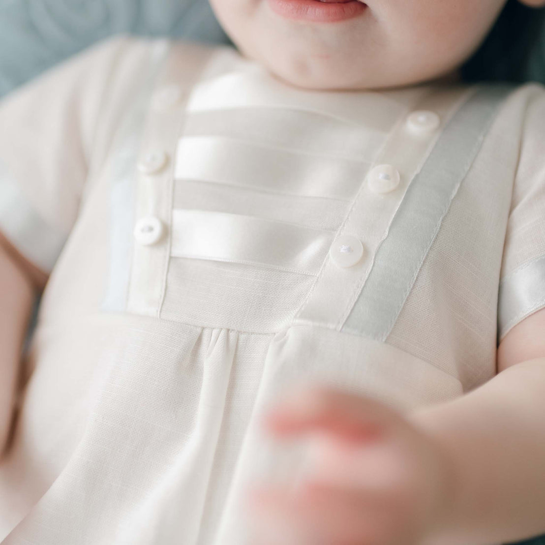 Close-up of a baby dressed in the Owen Linen Romper with button details, focusing on the outfit and partial view of the baby's hand.
