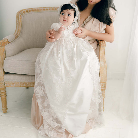 Baby girl sitting in mother's lap in silk and lace baby baptism gown and bonnet