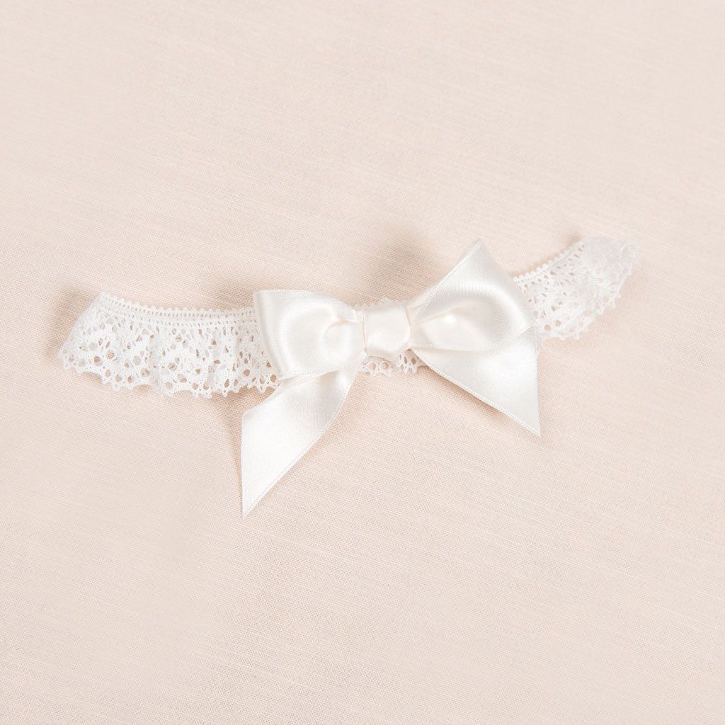 Flat lay photo of a lace headband with bow, part of a christening collection.