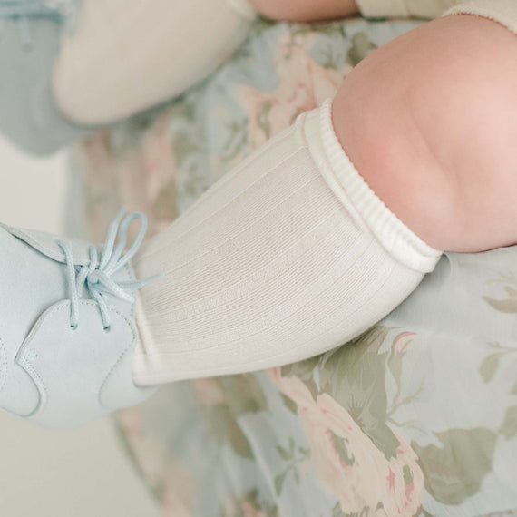 Photo of a baby wearing the Cream Ribbed Socks made from a soft cotton blend and featuring a ribbed pattern