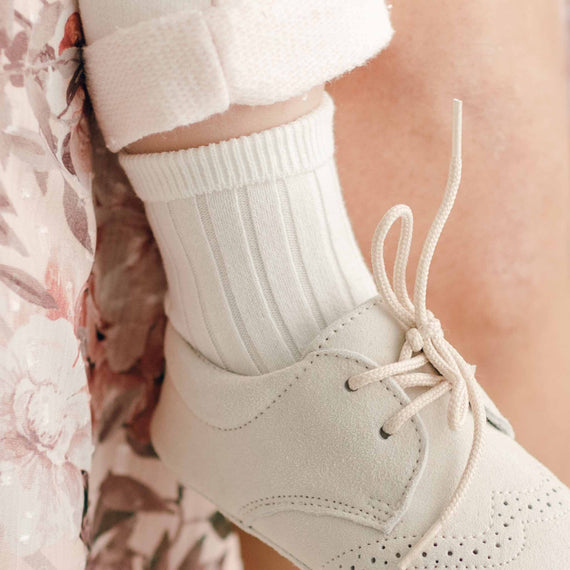 Close-up of a person's foot wearing a white, lace-up ankle brace over a Ribbed Sock, against a vintage floral fabric background. The brace appears to be providing support for mobility or injury recovery.