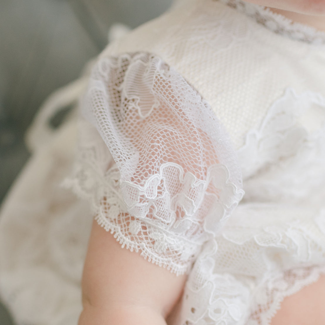 Close-up of the embroidered white floral lace detail on the sleeve of an Aria Bubble Romper, showcasing delicate patterns and textures.