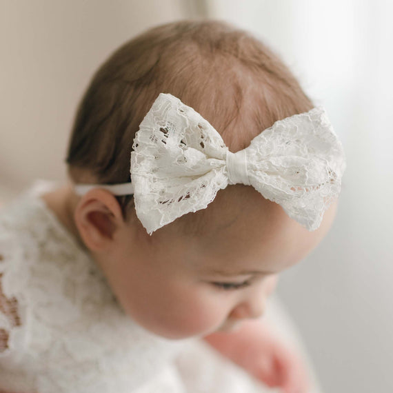 A close-up photo of a baby wearing the Rose Bow Headband, a delicate lace headband with a big lace bow, focusing on the headband and the baby's soft hair. The background is soft and blurred.