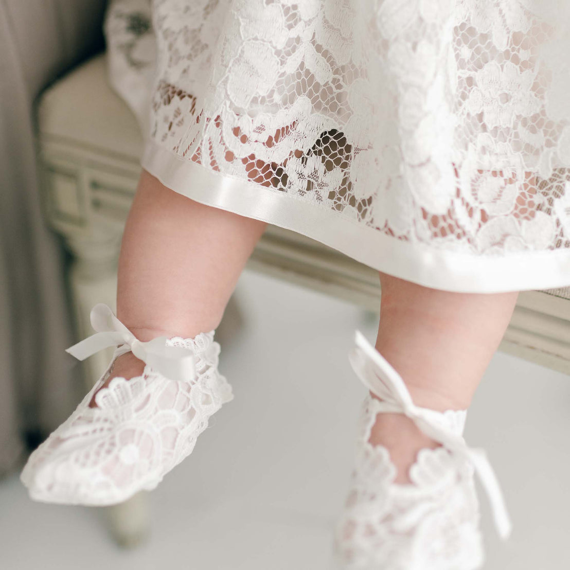 Close-up of a baby's feet dressed in the Rose Booties adorned with white silk ribbon ties, positioned above a wooden floor.