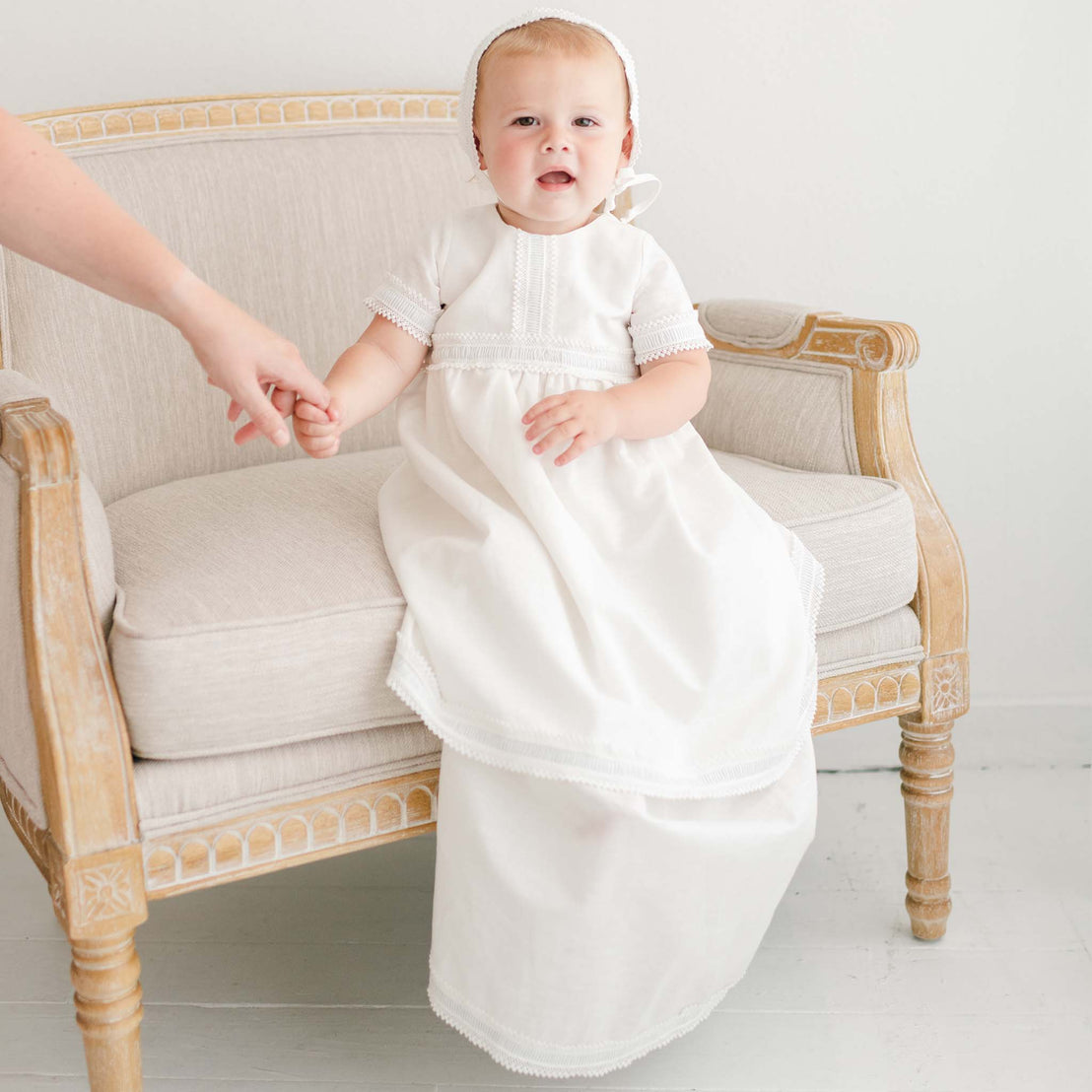 Baby boy holding moms hand, wearing a full-length linen boys baptism gown.