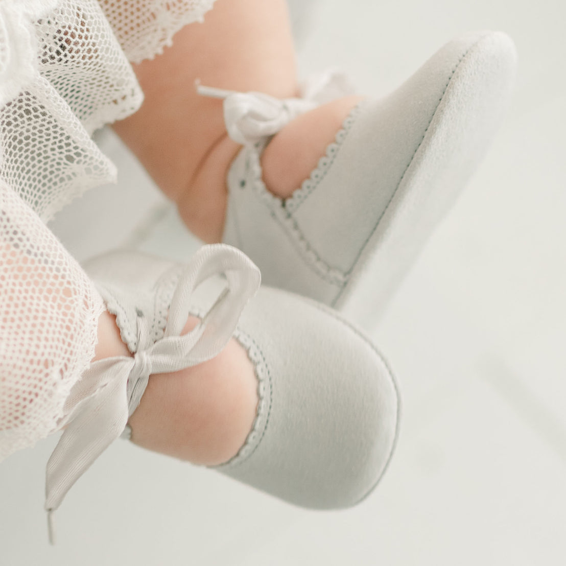 Baby girl wearing the dove grey Emily Suede Tie Mary Janes. Shoes are made with a soft suede with tie detail closure.