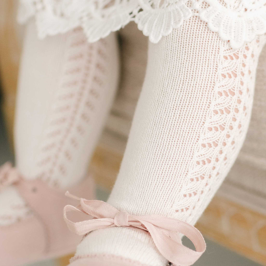 Close-up of a child's legs wearing white lace-trimmed Side Openwork Tights with pink bows, suggesting a christening or baptism.