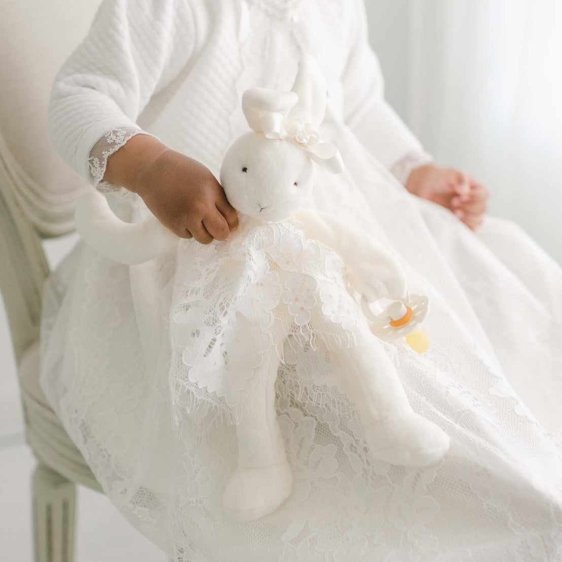 The silly bunny buddy, pictured with a baby girl wearing the Victoria Christening Gown. Baby girl is sitting on chair in photo studio.