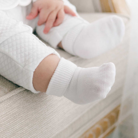 Close-up of a baby's feet wearing Boys Simple Socks, with the hands gently resting on a pair of baby white quilt pants.