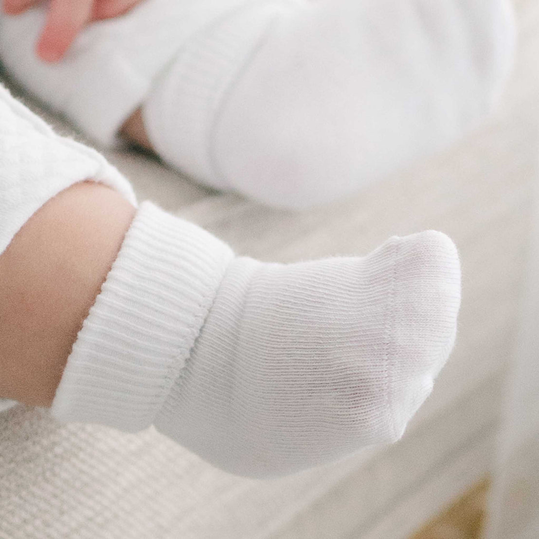 Close-up of a baby's tiny foot wearing a pair of Girls Simple Socks, resting on a soft beige surface, emphasizing the intricate texture of the sock and the plumpness of the foot.