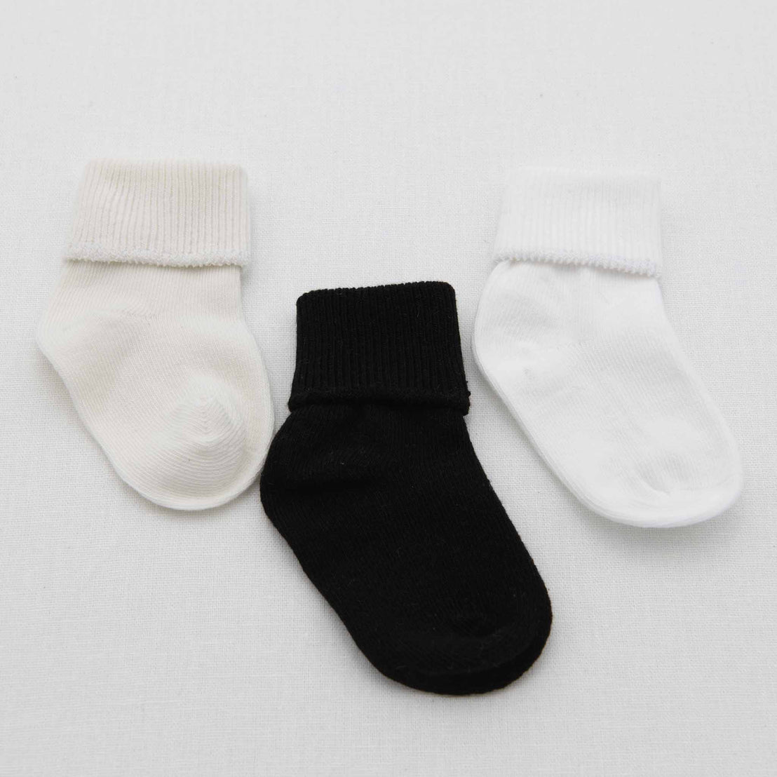 Three Boys Simple Socks, one in ivory, one in black, and another in white, are displayed on a light gray background.