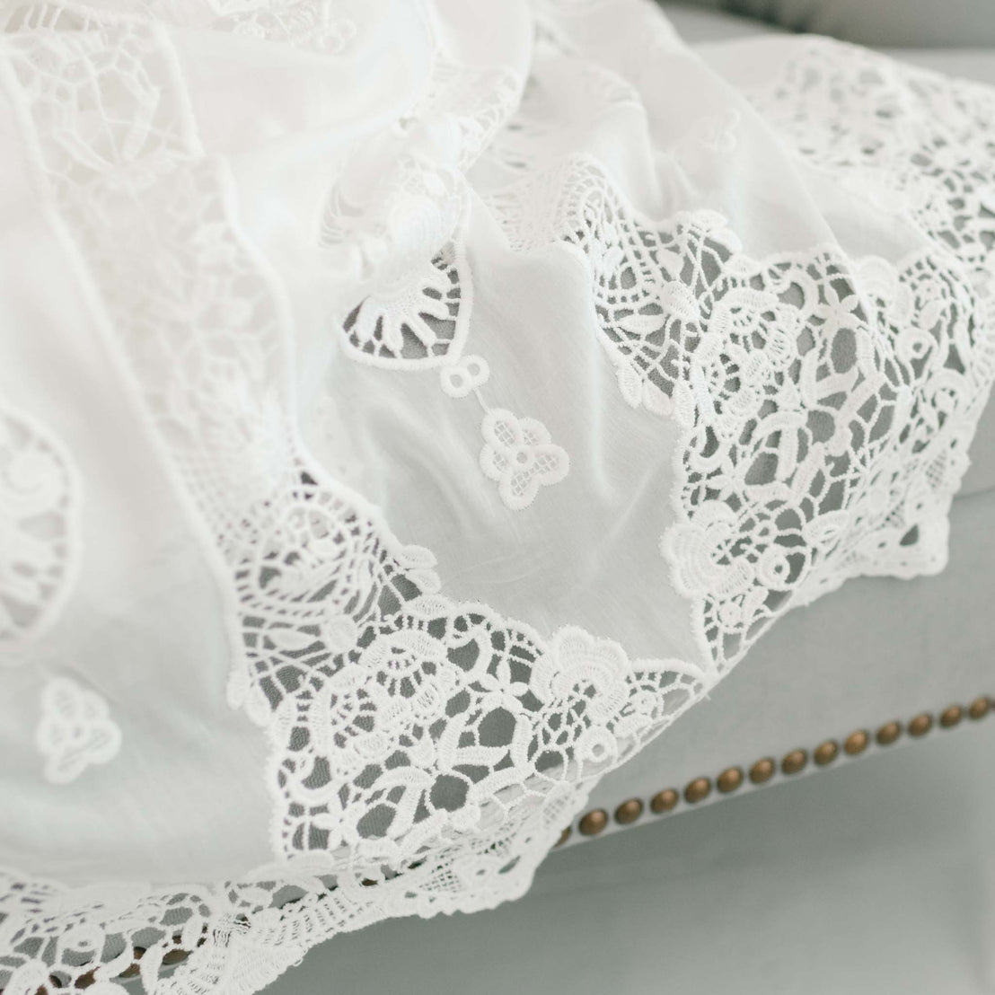 Close-up image of a white lace Grace Dress with intricate floral and heart designs, draped over an edge with a matte gray background.