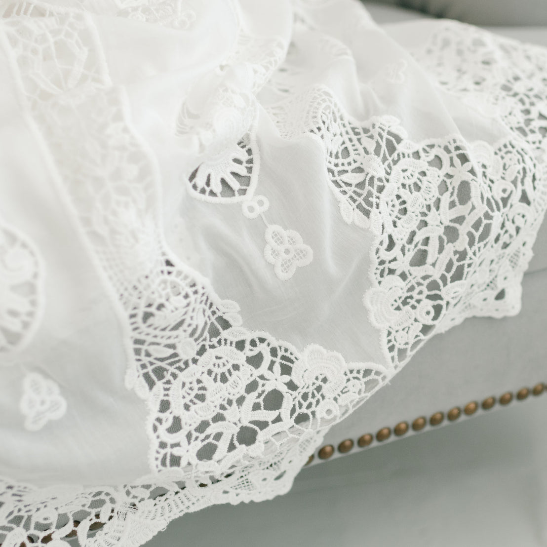 Close-up of a white lace Grace Christening Gown with intricate floral and heart patterns, featuring Venice inset, draped over a couch. 