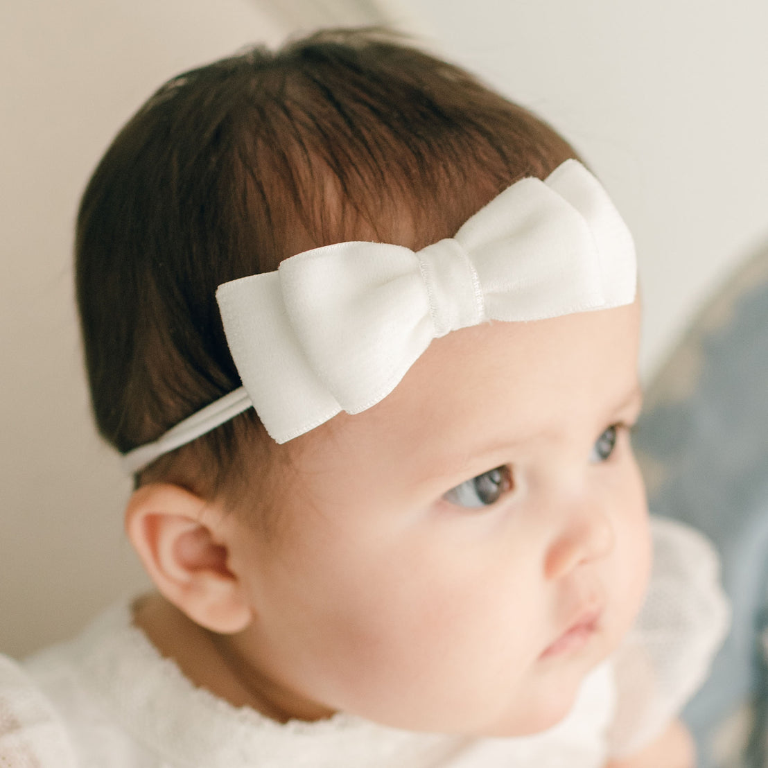 Baby girl wearing the white Emily Velvet Bow Headband with hand-stretched nylon band.