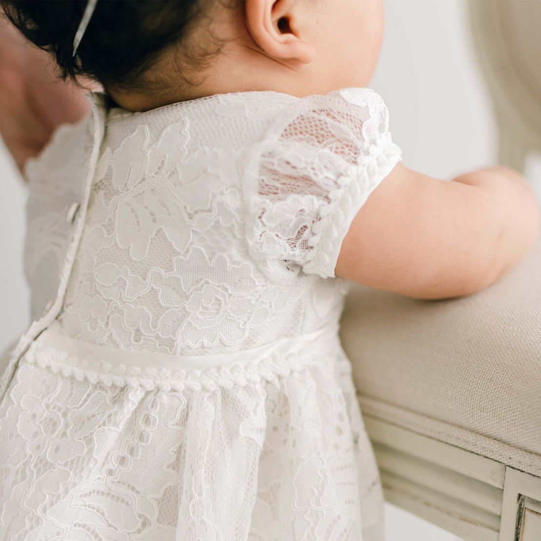 A close-up view of a baby wearing a Victoria Puff Sleeve Christening Dress, focusing on the delicate fabric details and the baby's tiny arm.