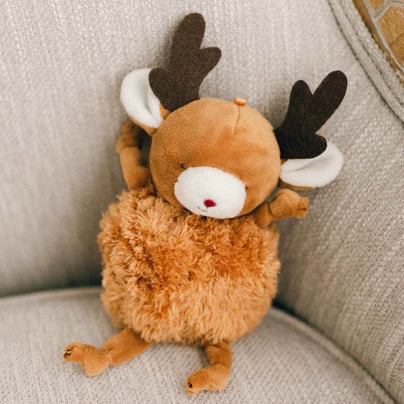 A Roly Poly Reindeer resembling a moose with brown fur and darker brown antlers sits comfortably on a light grey couch.