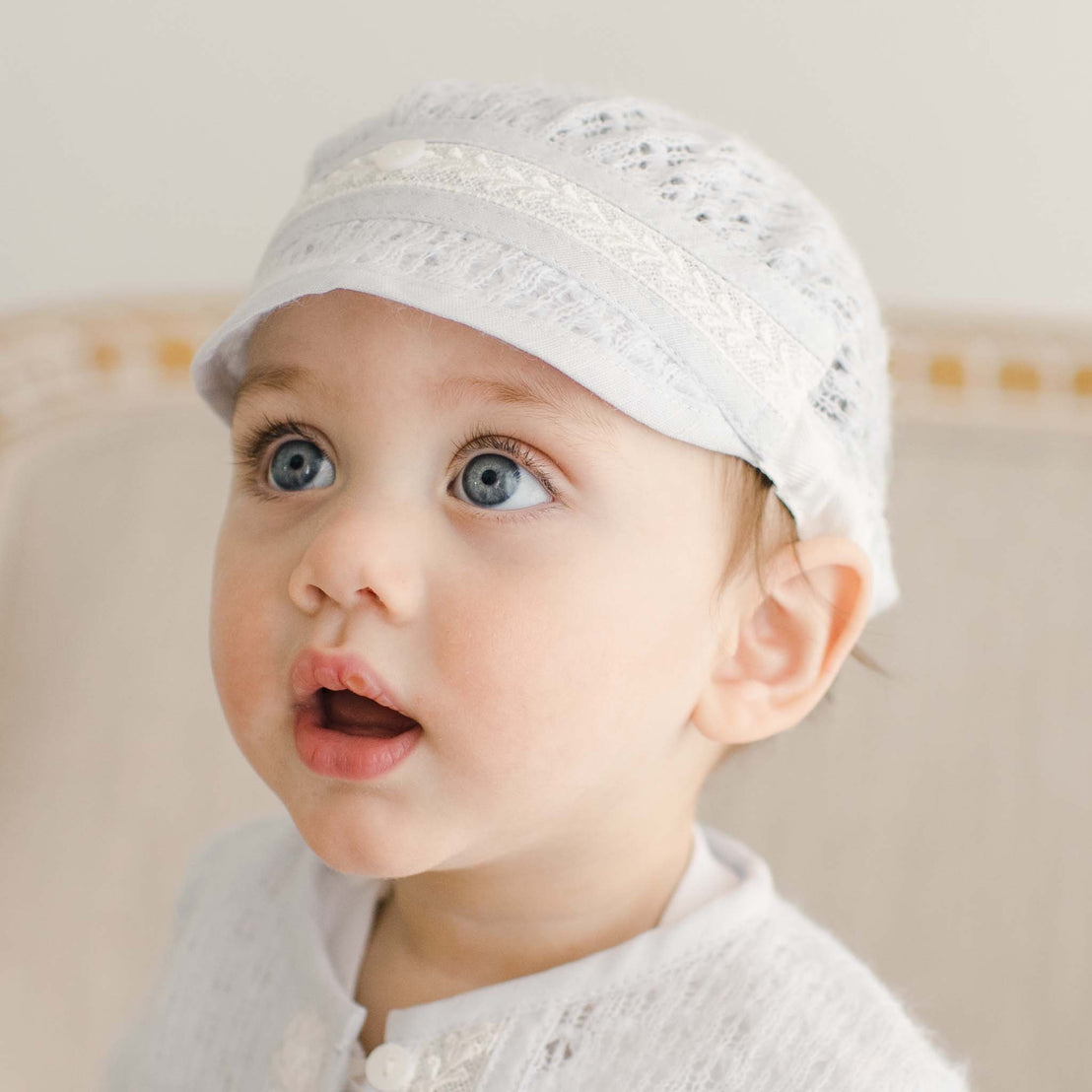 Baby boy wearing the Harrison Blue Knit Hat. The knit is detailed with soft blue linen/cotton blend edging and ivory Venice lace
