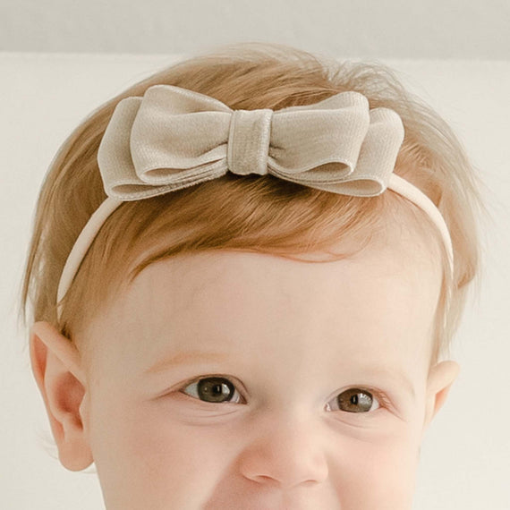 Baby girl with red hair wearing a velvet bow headband, part of the Adeline baptism collection.