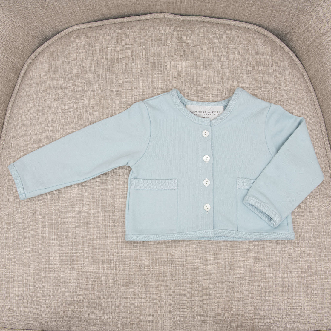 A light blue Ian French Terry Jacket with white buttons is neatly placed on a beige fabric chair.