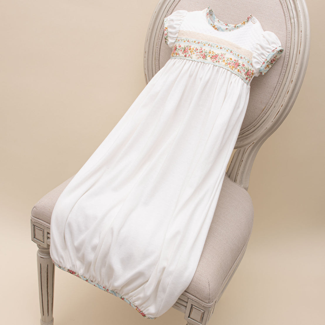 Flat lay of the Eloise Layette Gown in "Powder Blue". Details show the white pima cotton sleeves with white quilted textured cotton bodice. The gown features cotton lace, as well as, floral and striped cotton bodice details. Button closures are on both shoulders.