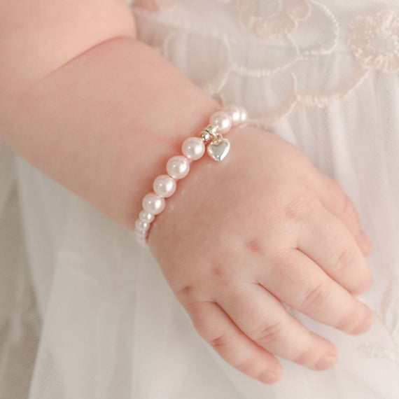 A close up of a baby girl's hand wearing the Pink Luster Pearl Bracelet with Silver Heart Charm  made from sterling silver.