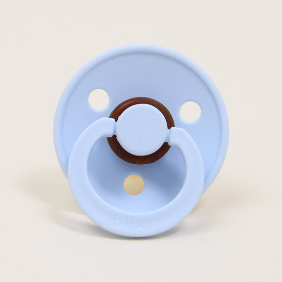A Bibs Pacifier 2 Pack | Baby Blue with a round wood accent on the pull tab, set against a neutral background. The brand "bibs" is visible on the front. This design is specifically crafted to