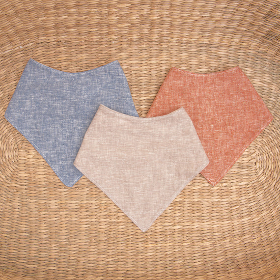 Flat lay photo of all three colors of the Silas Bandana Bib. The bibs are made from linen in three different colors: indigo, sand, and clay.