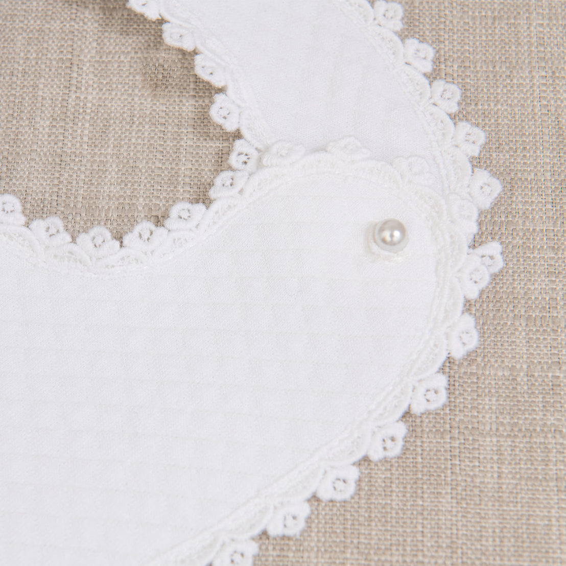 Close-up of the Mila Bib and its small pearl button enclosure on a beige fabric background
