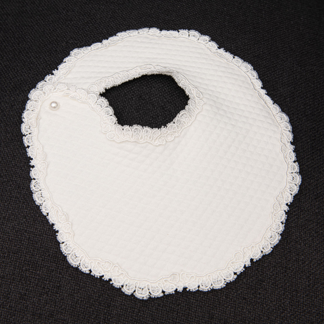 flat lay photo of baptism bib made of quilted cotton and floral edge lace.
