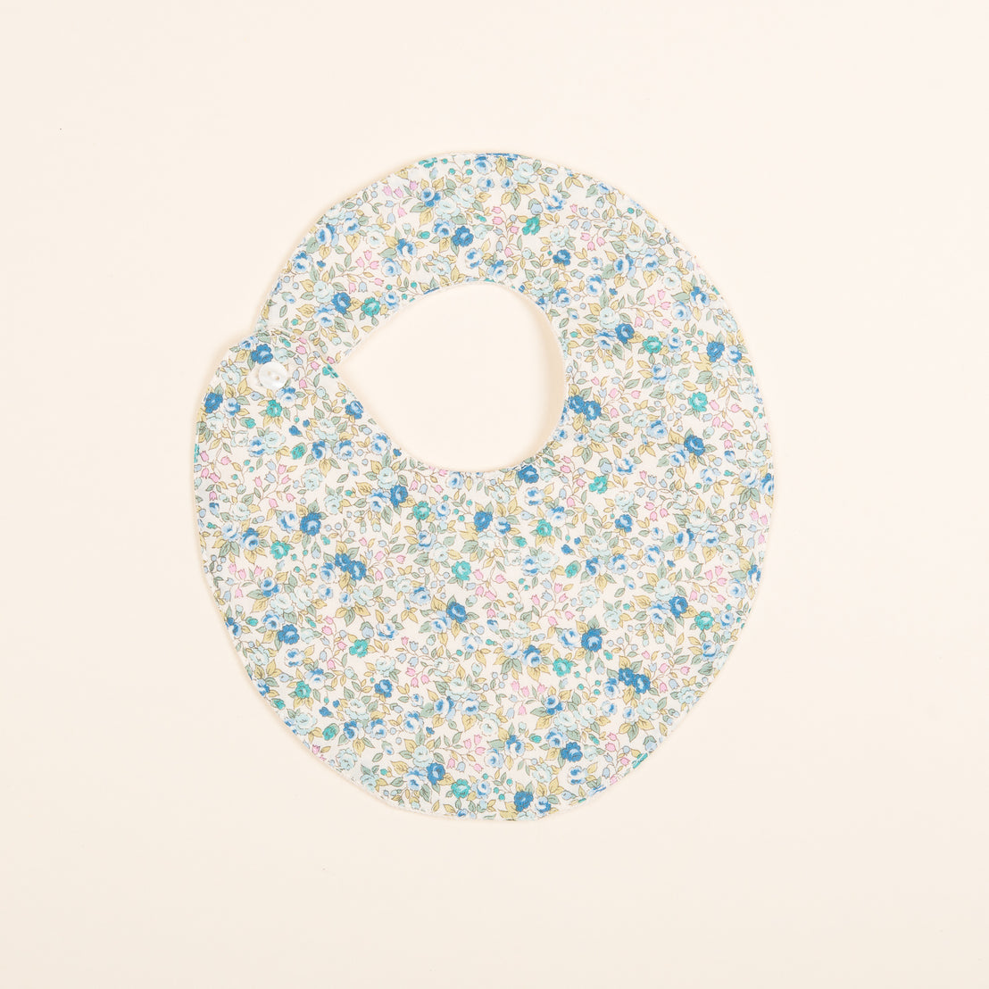 A round, heirloom Petite Fleur Bib with a cutout neck hole, featuring a small, intricate floral pattern in multiple colors on a neutral background.