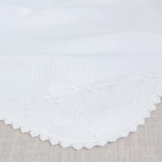 Close-up of upscale, heirloom white fabric with the name "Isla Personalized Blanket" embroidered in a delicate script, enhanced by a boutique lace border with floral patterns.