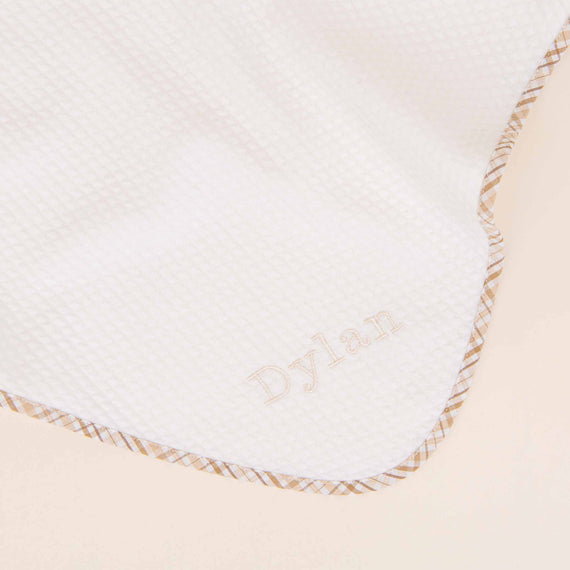 Close-up of a soft, white Dylan Personalized Blanket with a diamond texture pattern. The name "Dylan" is embroidered in the center with brown thread, bordered by a tan and white decorative trim.