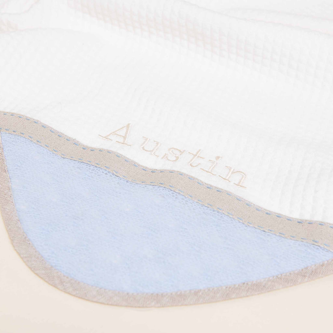 Close-up of an upscale, personalized Austin Blanket with the name "Austin" embroidered in elegant script on a blue and white fabric with a textured pattern, perfect for a coming home occasion.