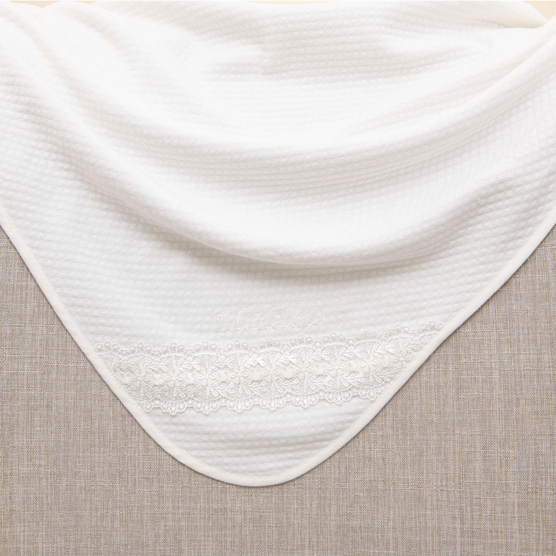 Madeline Blanket with delicate lace detailing along the edge, placed on a beige fabric background.