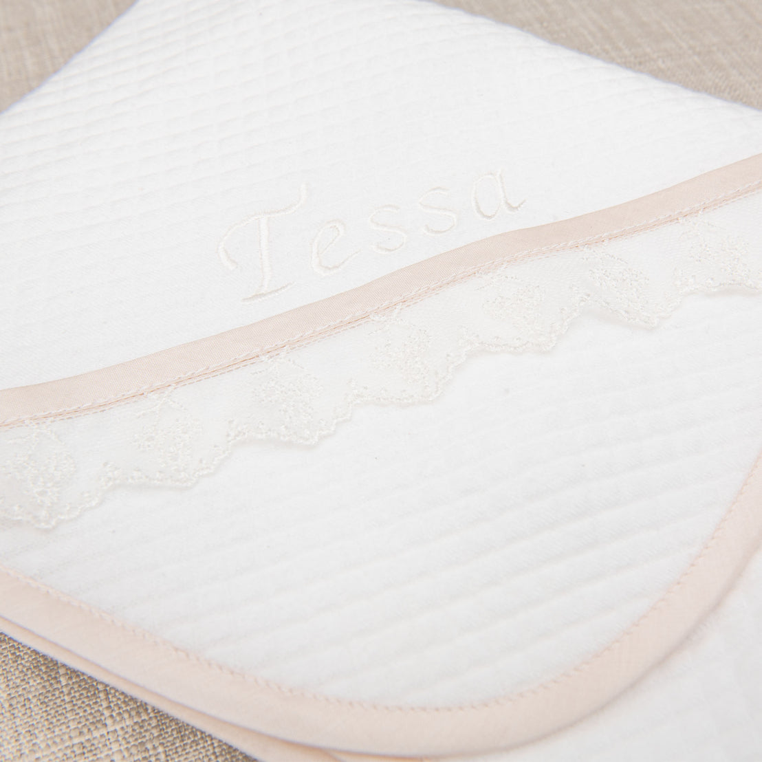 Flat lay photo of the Tessa Personalized Blanket made from a textured cotton in white and featuring a ivory embroidered lace trim and personalized name embroidery.