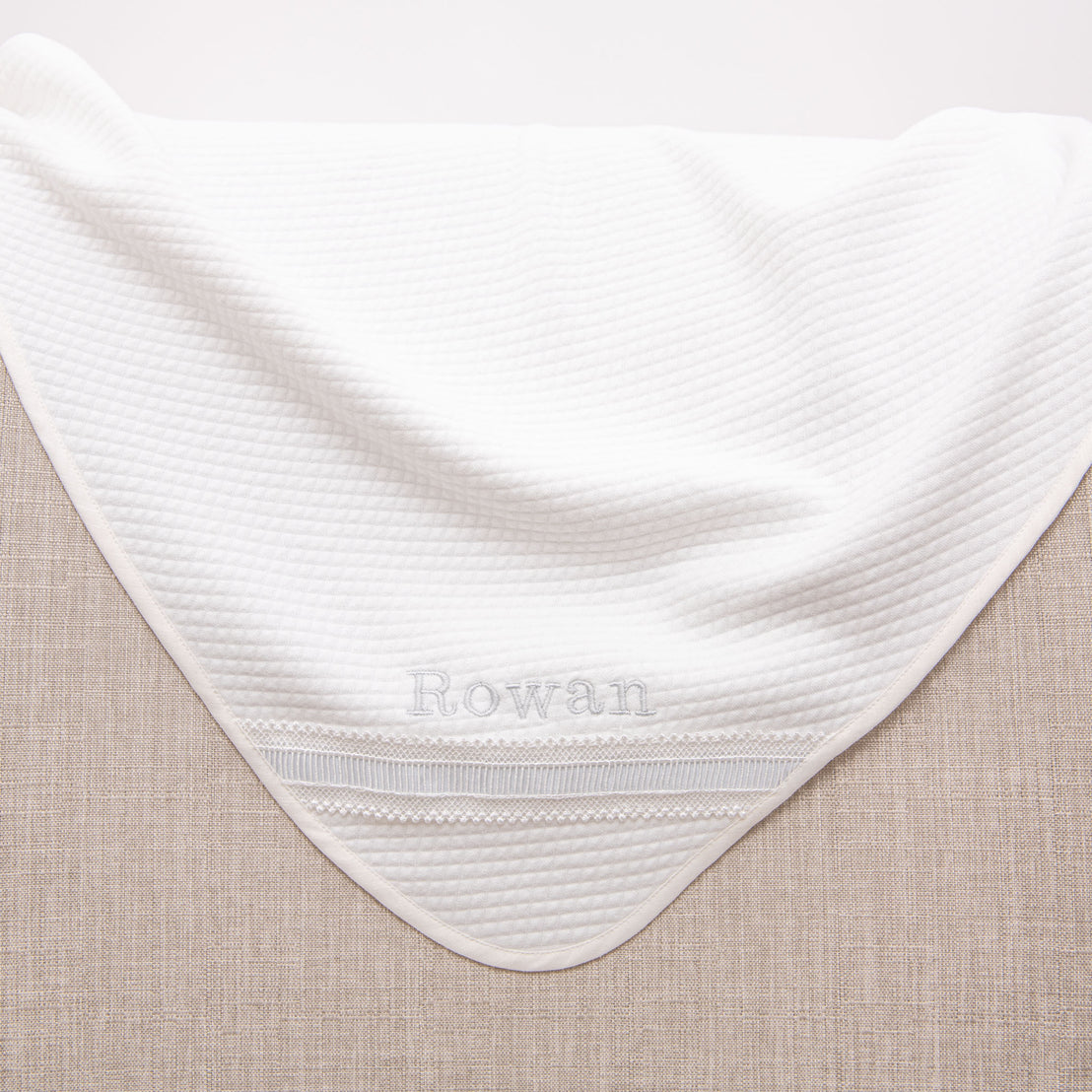 A personalized baby boy blanket embroidered with the name Rowan. Blanket is draped on the edge of a chair.