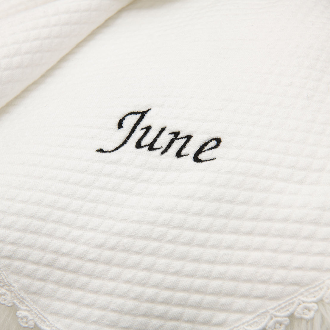 Close-up of a white textured cotton June Personalized Blanket with a waffle weave texture, featuring the name "June" embroidered in black script font.