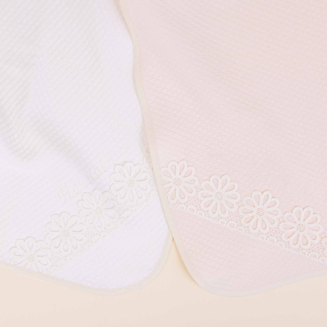 Two Hannah Newborn Gift Sets, one white and one pink, both embellished with floral lace details and part of a vintage baby clothes collection, overlapping slightly against a soft beige background.