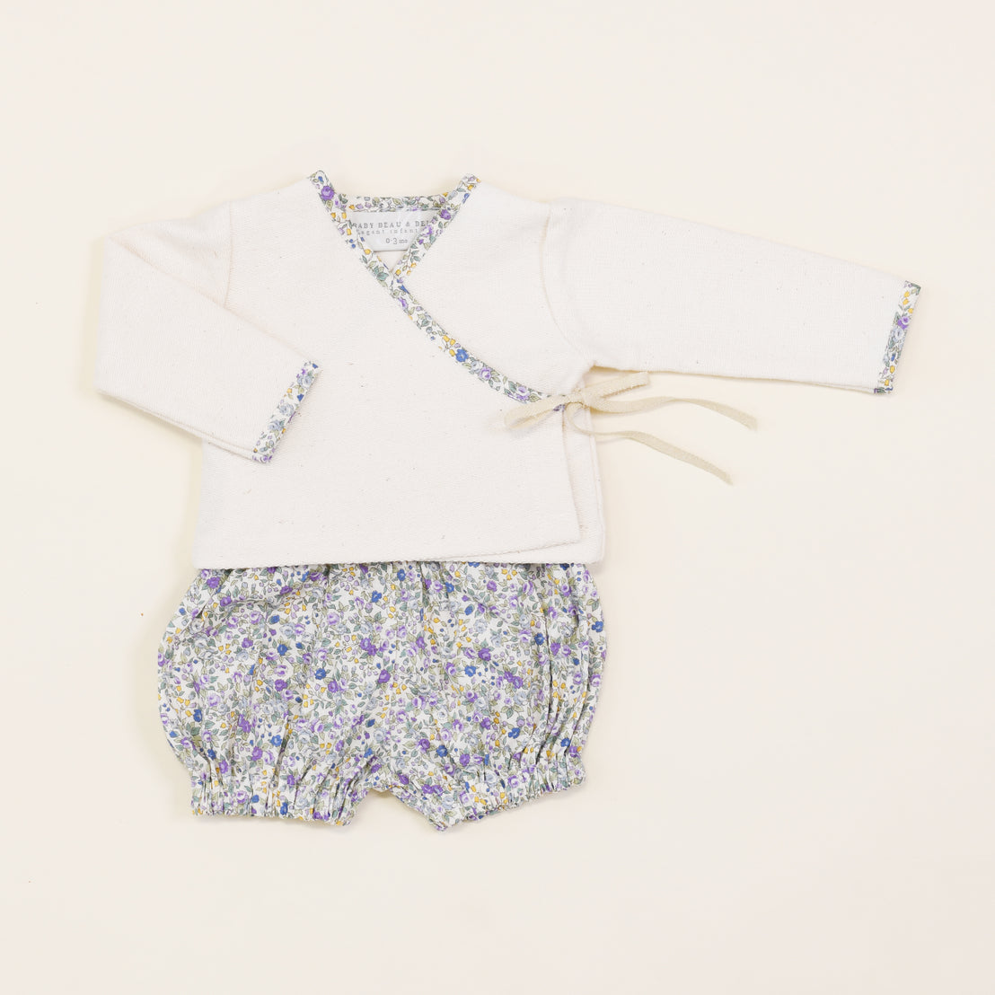 A baby's outfit consisting of the Petite Fleur Wrap Top & Bloomers, displayed on a plain beige background.