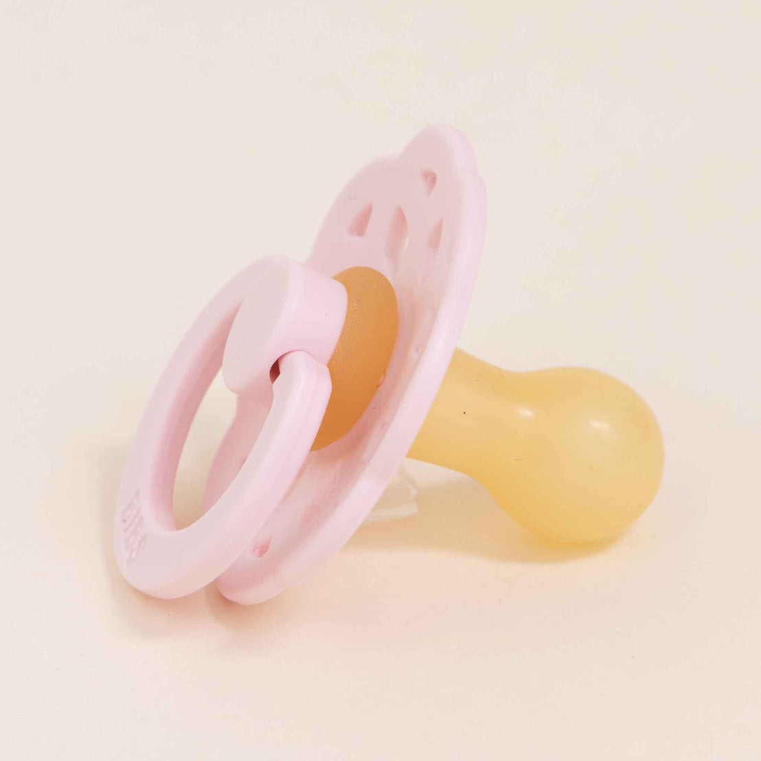 A pink and yellow Bibs Lace Pacifier made from natural rubber, lying on a light beige background.