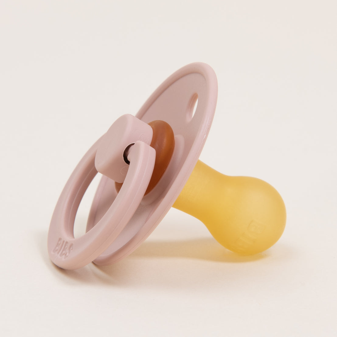 A pink Bibs Pacifier in Blush with a translucent rubber nipple and handle, isolated on a light beige background.