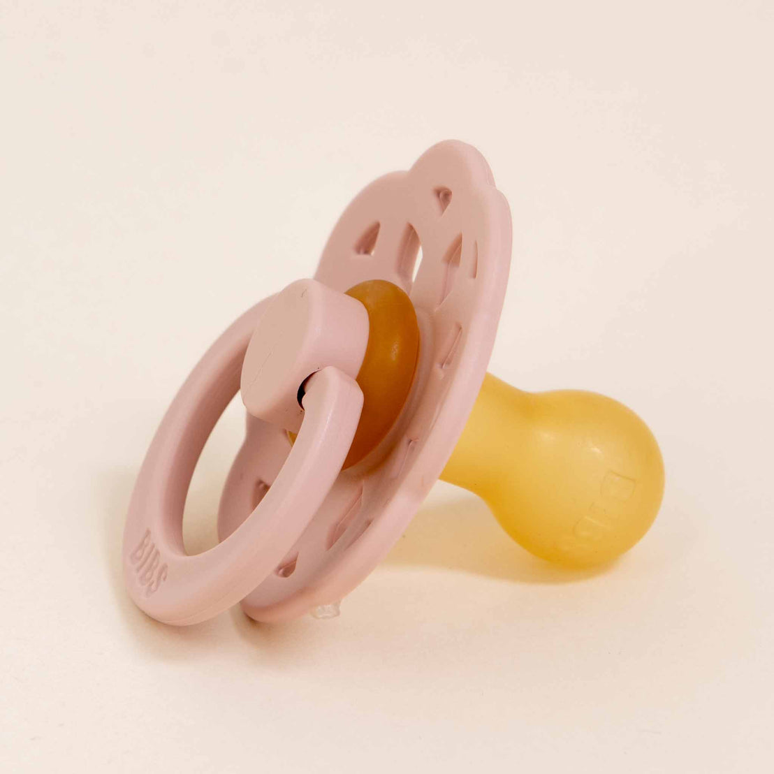 A pink and yellow Bibs Lace Pacifier in Blush against a plain, light background.