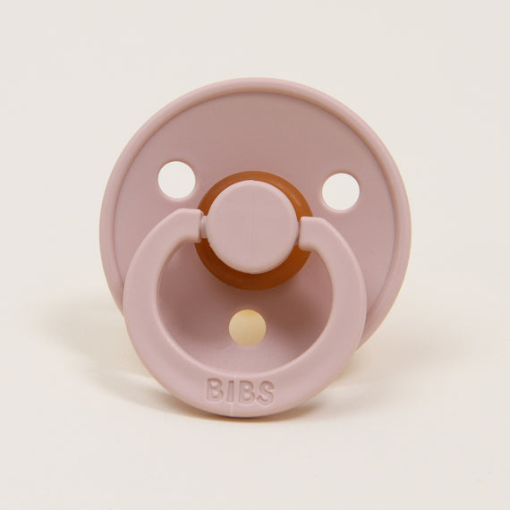 A Bibs Pacifier 2 Pack | Blush with a round shield and two ventilation holes, featuring a brown silicone nipple and a ring handle, set against a plain white background.