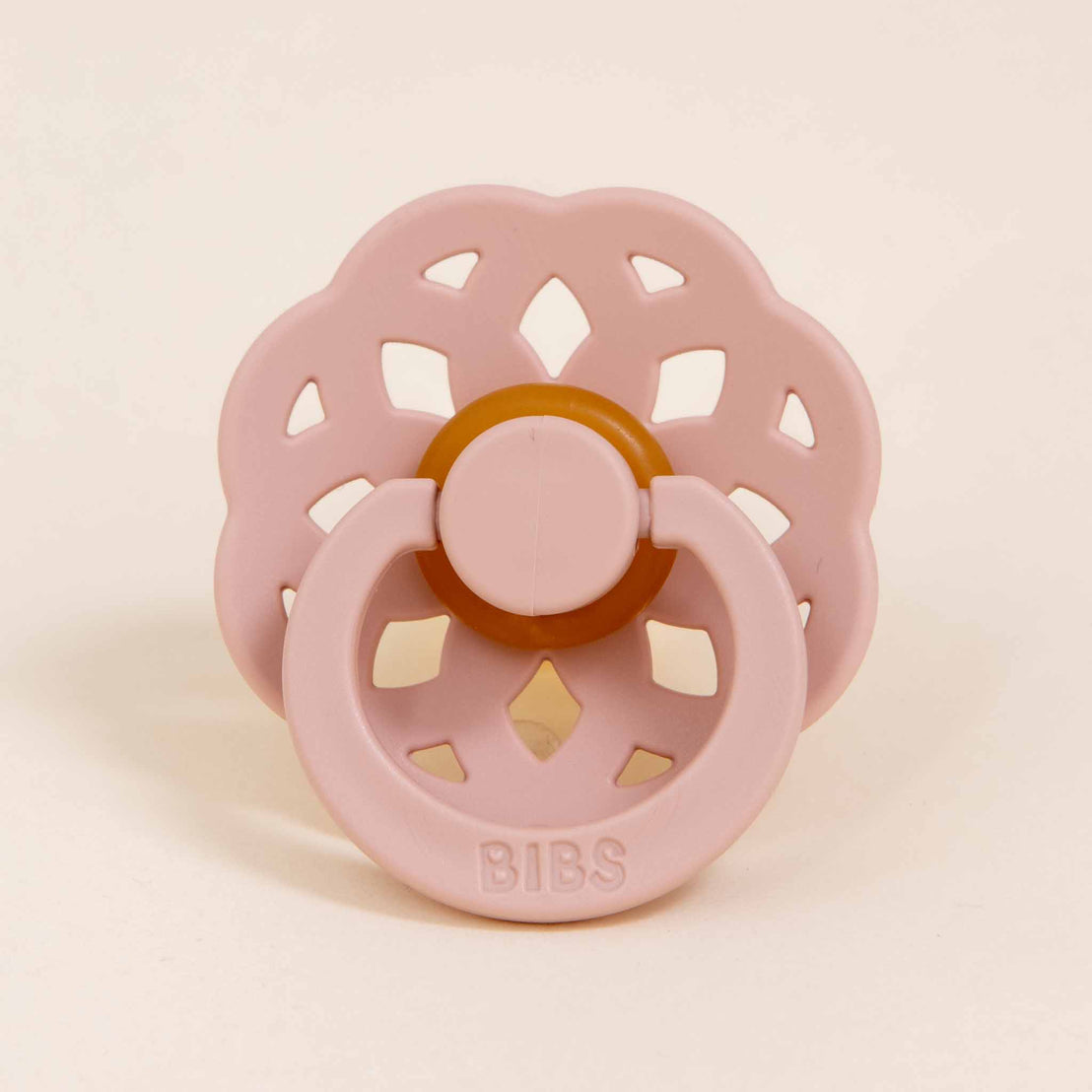 A light pink Isabella Pacifier Set with a vintage ornate pattern and a circular handle, labeled "bibs" on a beige background.