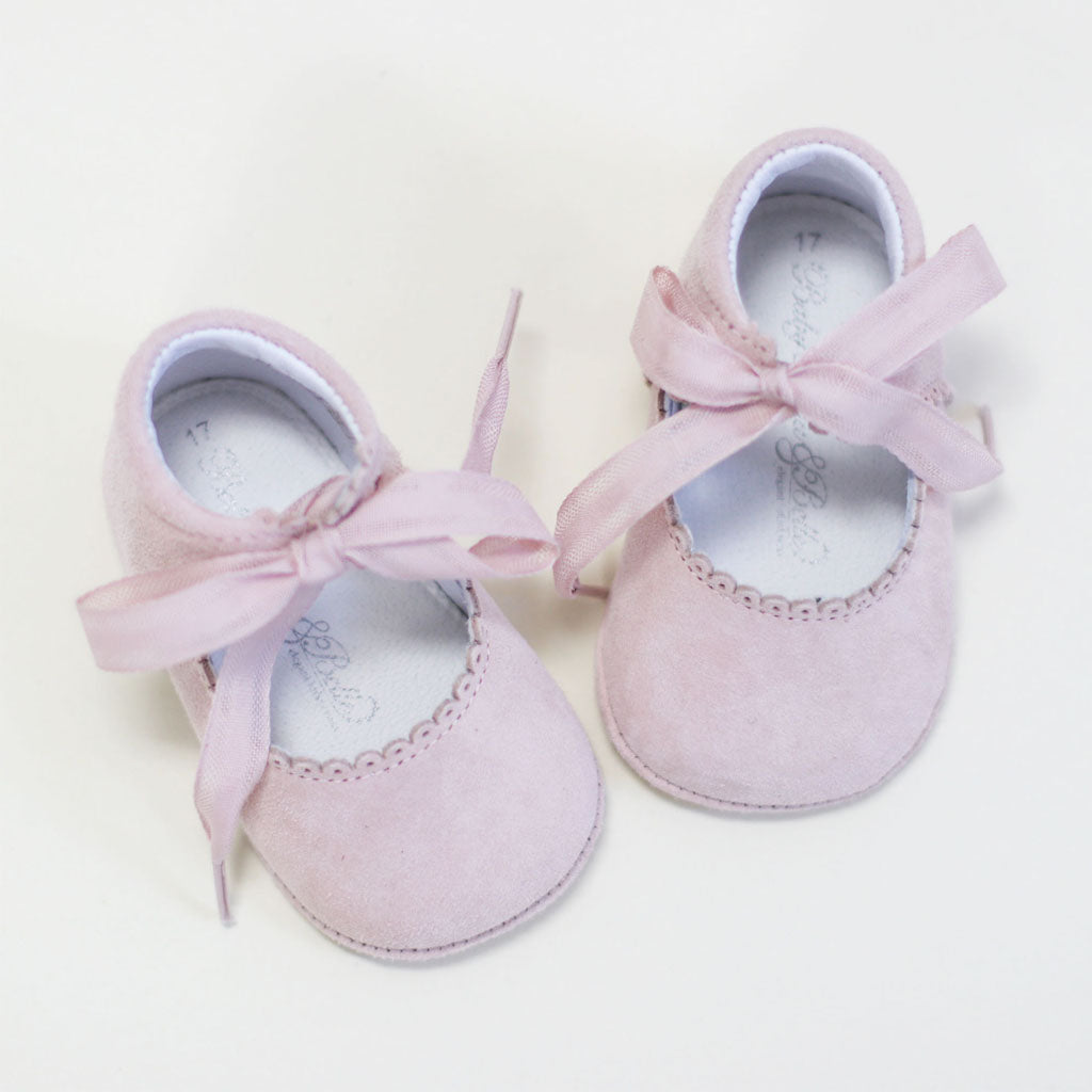 A pair of Blush Suede Tie Mary Janes with ribbon ties and decorative edging, perfect for a christening or baptism, on a white background.