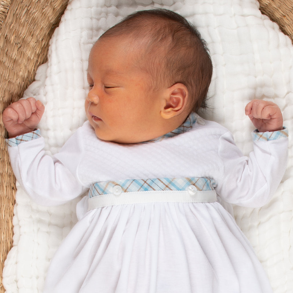 A newborn baby sleeps peacefully on a white blanket inside a basket, wearing the Mason Newborn Gift Set, prepared for his baptism.